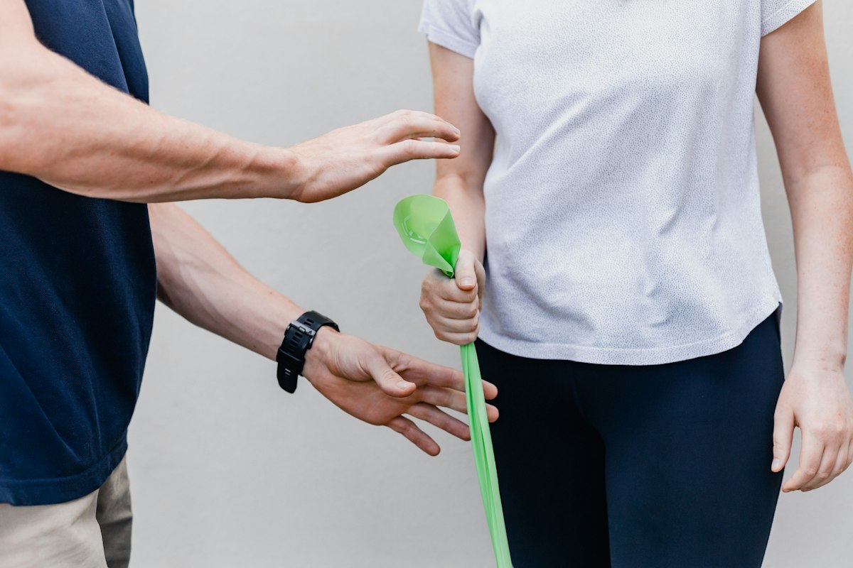 A patient stretching an exercise band with a physiotherapist guiding the movement