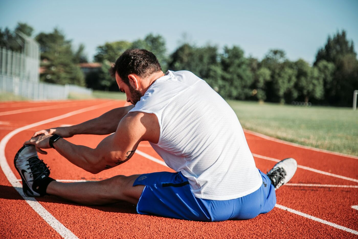 A runner stretching his hamstring on a running track