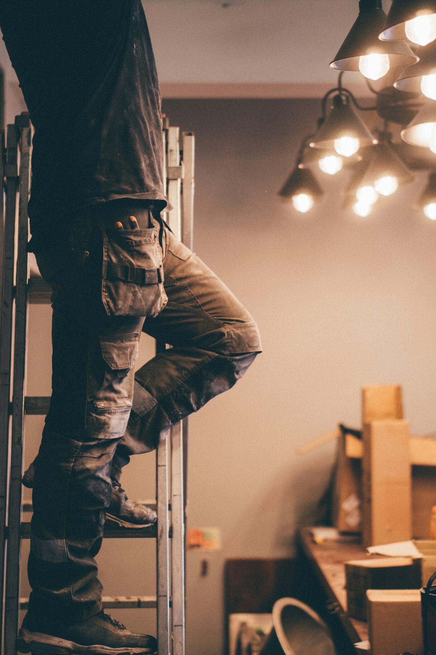 An electrician on a ladder fitting a row of pendant lights