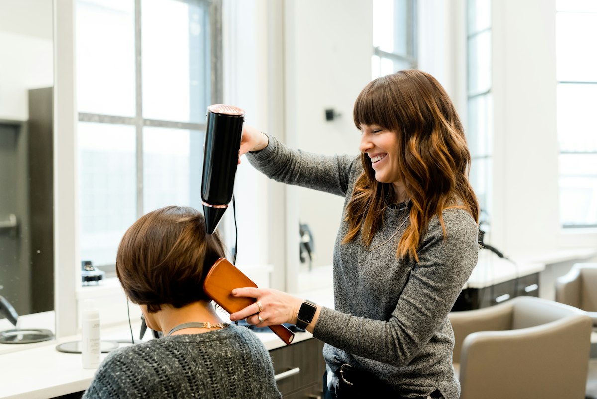 A stylist blow-drying a client's hair and smiling