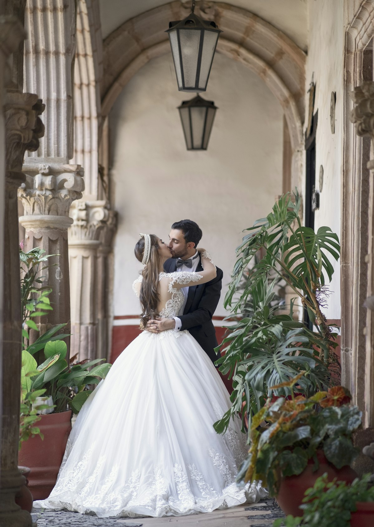 A couple kissing under stone arches between tall plants