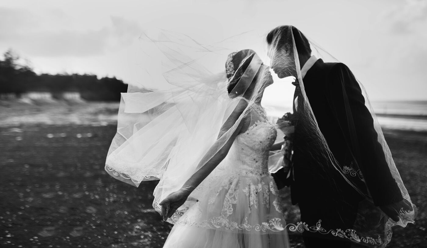 Black and white photo of a couple kissing as the veil blows in the wind