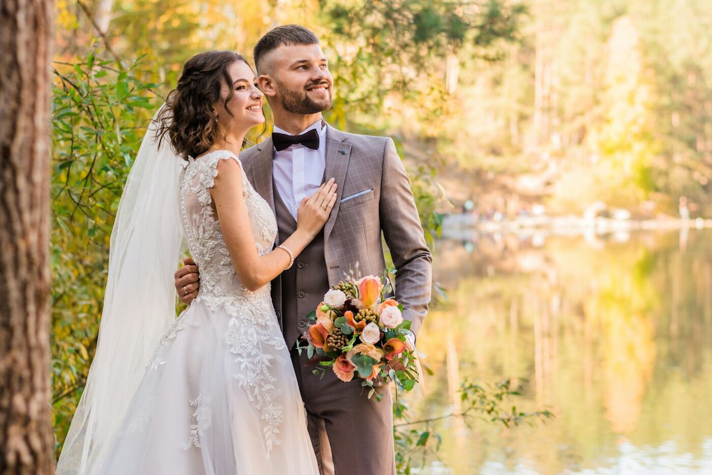 A bride and groom by a lake in autumn colours