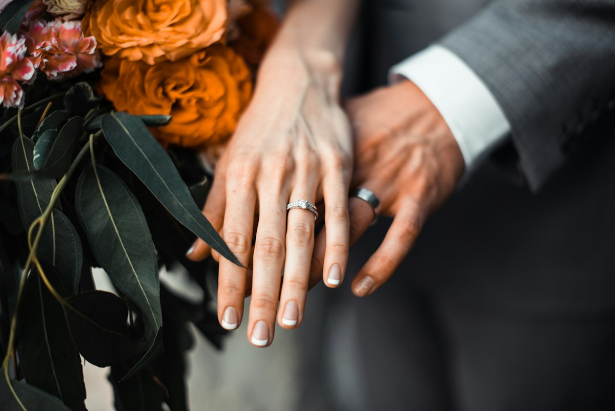The couple's hands with their wedding rings, next to a bouquet of orange flowers
