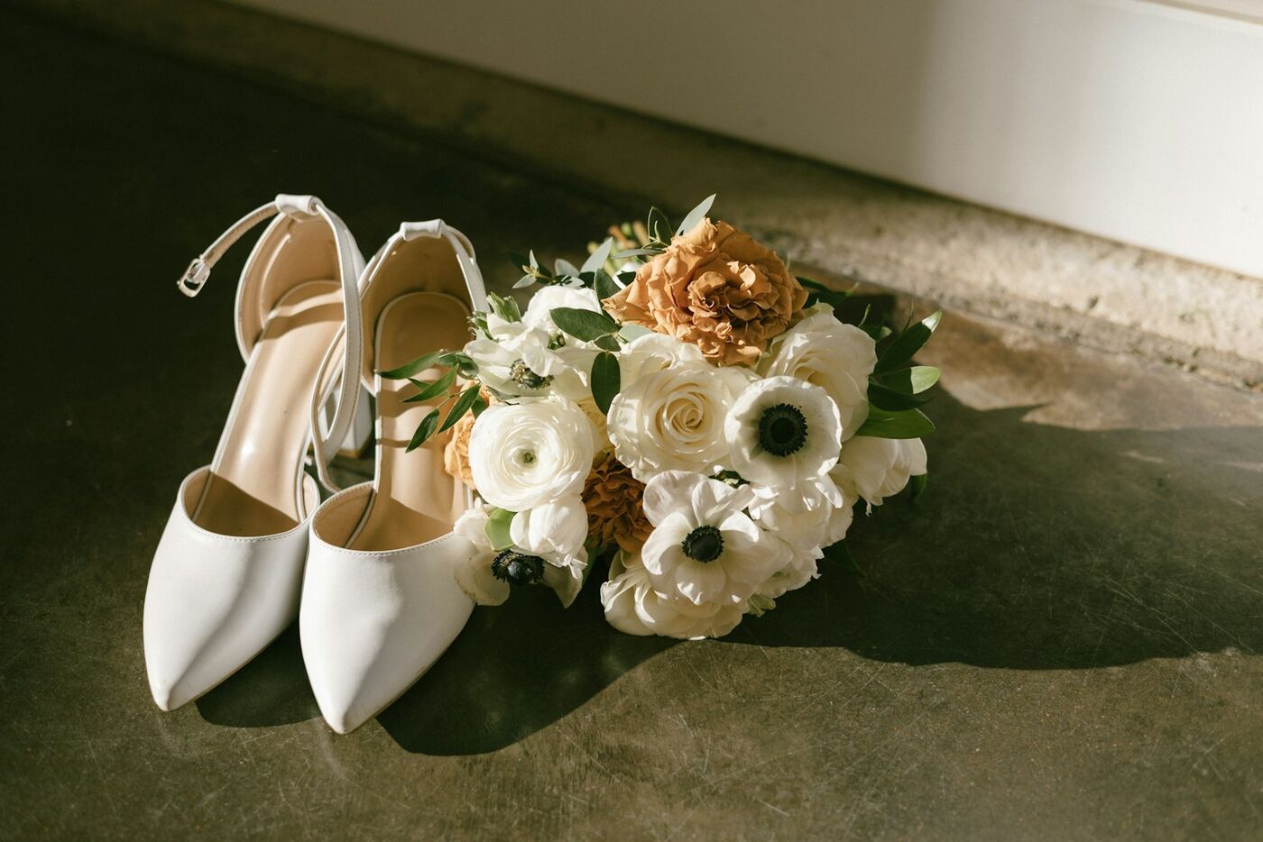 White wedding shoes beside a bouquet of white flowers