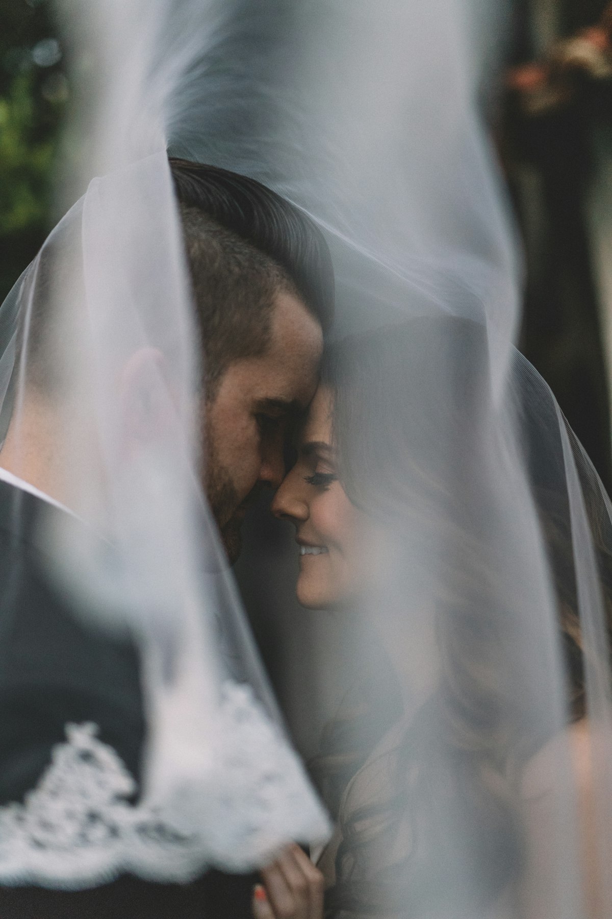 A bride's face half hidden behind her veil, close to her partner