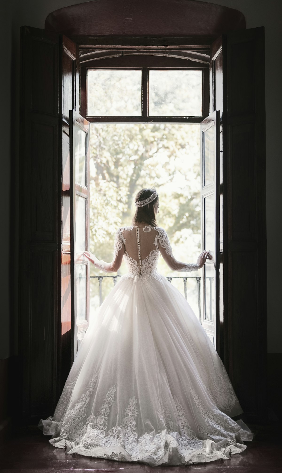 A bride in her dress standing at an open window in soft light